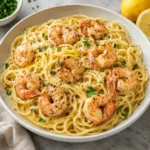 Lemon shrimp pasta with creamy spaghetti, pink shrimp, Parmesan, parsley, and lemon zest served in a shallow ivory bowl on a bright white marble-style surface, softly lit with natural light.