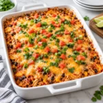 easy chicken burrito casserole in a white ceramic baking dish on a bright white marble surface, with shredded chicken, rice, black beans, corn, melted Monterey Jack cheese, and fresh cilantro in a square main recipe photograph.