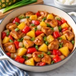 Pineapple chicken stir-fry served in a cream enamel skillet on white marble, with glossy browned chicken, pineapple chunks, red bell pepper, onion, scallions, and sticky sauce.