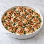 Baked chicken ricotta meatballs nestled in creamy spinach Alfredo sauce in a white ceramic baking dish, with golden-browned tops on a bright white marble surface.