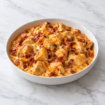 Creamy buffalo chicken and browned bacon in a white ceramic bowl on white marble.