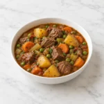 Slow cooker beef stew with tender beef and vegetables in a white ceramic bowl on bright white marble.