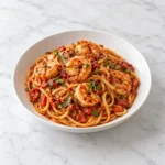 Shrimp fra diavolo linguine with fire roasted tomato sauce and herbs in a white ceramic bowl on white marble.