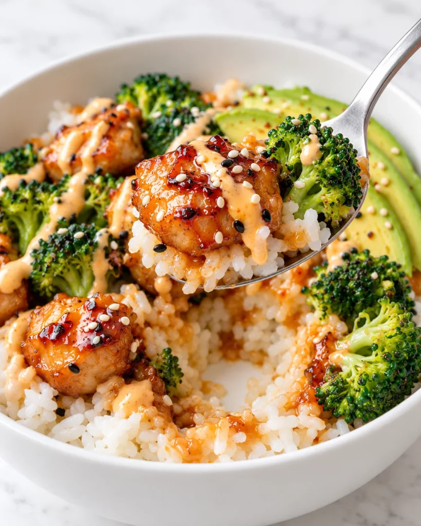 A spoon lifts sticky chicken, rice, and broccoli from a white ceramic bowl, showing the saucy scoop and disturbed rice beneath